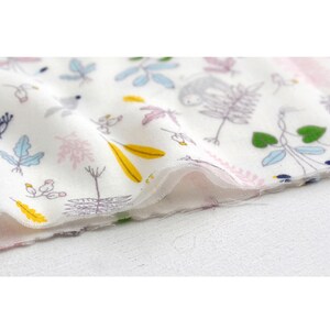 May include: White fabric with a repeating pattern of pink, yellow, and blue leaves, green vines, and a sloth. The fabric is folded over on itself.