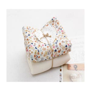 May include: A stack of two fabric squares, one with a floral print and the other plain white, tied together with twine and a white lace doily.