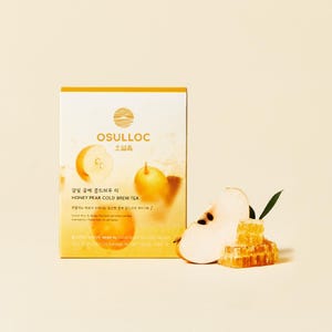 Peut inclure: Une boîte jaune de thé glacé Osulloc Honey Pear, une poire tranchée et un rayon de miel. La boîte contient du texte en coréen et en anglais. La poire est jaune clair avec des graines foncées. Le rayon de miel est jaune doré.