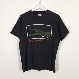 May include: Black t-shirt with a graphic print of a green B-25 Mitchell bomber plane in a white frame. The text "B-25 Mitchell" is printed below the plane in red.