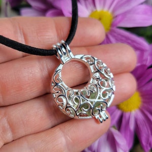 May include: A silver locket necklace with a delicate filigree design. The locket is open and has a small green stone inside.