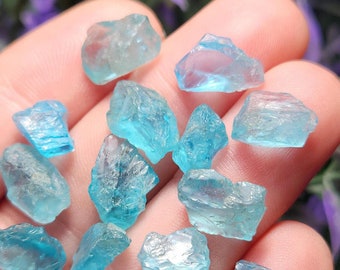 May include: A collection of raw aquamarine crystals in various shapes and sizes. The crystals are a light blue color and have a translucent appearance.