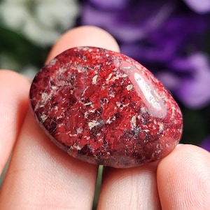 May include: A smooth, red and white tumbled stone with a speckled pattern.