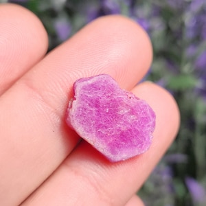 May include: A pink ruby crystal with a rough, faceted surface.