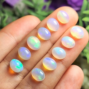 May include: A collection of oval-shaped opals, each displaying a unique play of color. The opals range in color from milky white to translucent, with flashes of green, blue, and yellow. The gemstones are displayed on a hand.