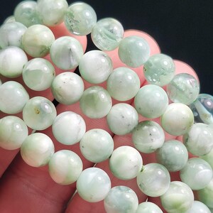 Peut inclure: Gros plan de plusieurs bracelets de perles de pierres pr&eacute;cieuses vert clair. Les perles rondes ont un aspect marbr&eacute; avec des variations de couleur. Les bracelets sont tenus dans une main sur fond sombre.