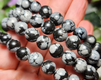 May include: Three black and white speckled stone bracelets stacked on top of each other. The bracelets are made of round beads.