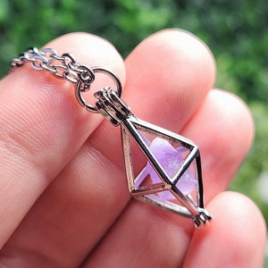 May include: A silver cage pendant necklace with a purple crystal inside. The cage is shaped like a diamond and has a delicate chain.
