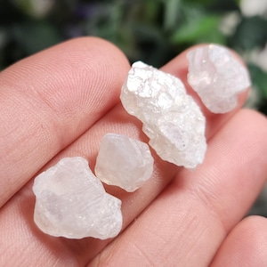May include: Four small, white, iridescent, rough, natural, raw, gemstone crystals. The crystals are translucent and have a pearly sheen.