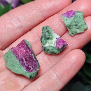 May include: Three green and pink rough gemstones. The gemstones are irregularly shaped and have a mottled green and pink color.