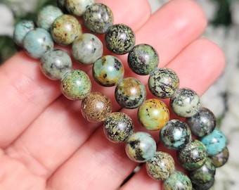 May include: Three turquoise beaded bracelets with green, brown, and black marbling. The bracelets are stacked on top of each other and are being held in a hand.