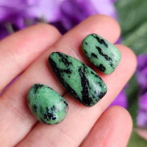 May include: Three green and black gemstone tumbled stones. The stones are smooth and have a natural, organic shape.