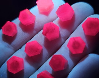 May include: A collection of 11 bright pink, faceted, hexagonal crystals. The crystals are arranged in a semi-circle on a hand.