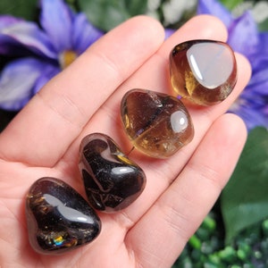 May include: Four tumbled smoky quartz stones in various shades of brown and black. The stones are smooth and polished, with a slight sheen.