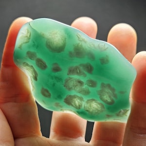 May include: A green, translucent, irregularly shaped stone with white inclusions. The stone is smooth and polished.
