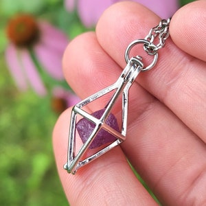 May include: A silver cage pendant necklace with a purple crystal inside. The cage is shaped like a diamond and has a delicate chain.