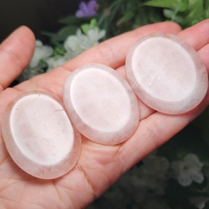 May include: Three oval-shaped, translucent, white, polished, crystal stones. The stones are smooth and have a slightly cloudy appearance.
