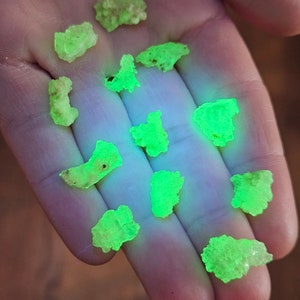 Peut inclure: Une collection de petites pierres fluorescentes vertes. Les pierres sont de forme irrégulière et ont une texture rugueuse. Elles brillent sous une lumière noire.