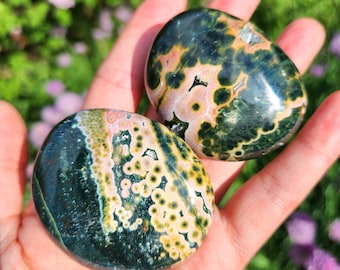 May include: Two green, yellow and pink ocean jasper palm stones. The stones are smooth and polished, with a variety of patterns and colours.