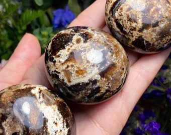 May include: Three brown and white tumbled stones with a marbled pattern. The stones are smooth and polished.