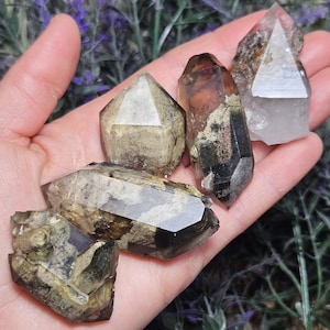 May include: A collection of raw, natural quartz crystals in various shapes and sizes. The crystals display a range of colors, including clear, brown, and smoky hues. Some crystals have visible inclusions and unique patterns, showcasing their natural beauty.