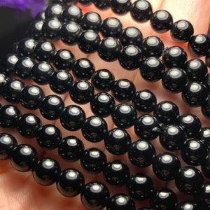 May include: A close-up of multiple strands of black onyx beads. The beads are round and smooth, with a high polish.