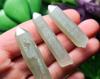 May include: Three light green crystal points with a shimmery, iridescent finish. The points are arranged in a row, with the tips pointing to the right.