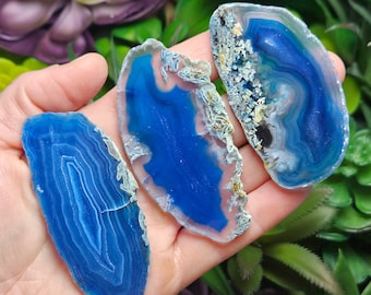 May include: Three polished blue agate slices with detailed banding patterns. The slices vary in shape and size, displaying a range of deep blue hues with white and tan accents. These natural gemstones are suitable for jewellery making or display.