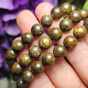 May include: A close-up of a bracelet made of dark brown wooden beads with gold flecks. The beads are round and have a smooth, polished finish.