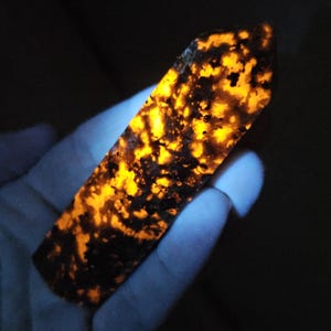 May include: A polished, elongated crystal point displaying a striking contrast between deep black, opaque inclusions and vibrant, glowing orange patches that illuminate the stone's surface, creating a mottled, fiery appearance throughout the structure.