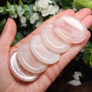 May include: A stack of six smooth, oval-shaped rose quartz stones. The stones are pale pink and translucent.