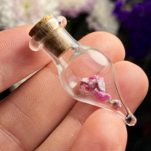 May include: A small glass bottle with a cork stopper, containing a cluster of pink ruby crystals.