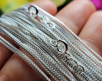 May include: A close-up of a stack of silver chain necklaces, each with a different size and style of chain. The chains are arranged in a fan shape, with the smallest chain at the top and the largest chain at the bottom.