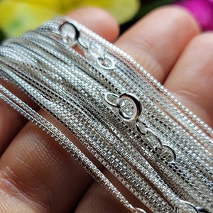 May include: A close-up of a stack of silver chain necklaces, each with a different size and style of chain. The chains are arranged in a fan shape, with the smallest chain at the top and the largest chain at the bottom.