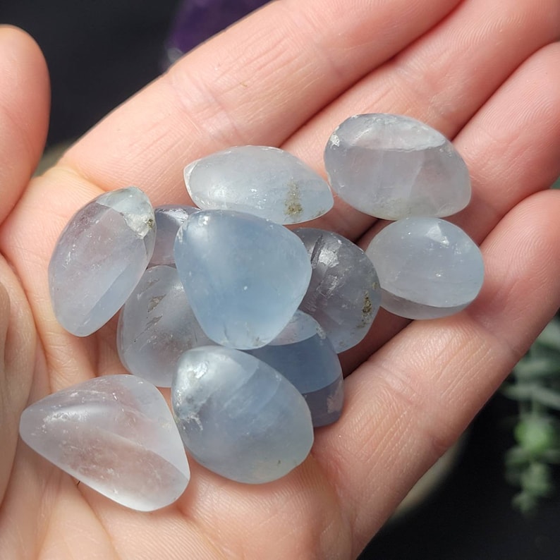 May include: A collection of light blue tumbled celestite stones. The stones are smooth and polished, with a slightly cloudy appearance.