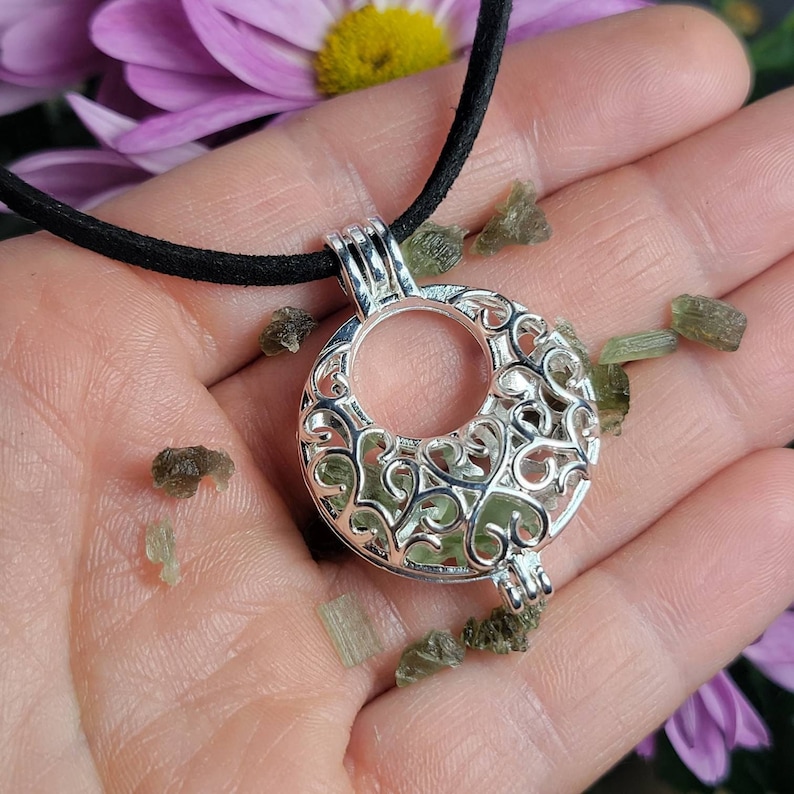 May include: A silver filigree cage pendant necklace with a green aventurine crystal inside. The necklace is on a black cord and is surrounded by loose green aventurine crystals.