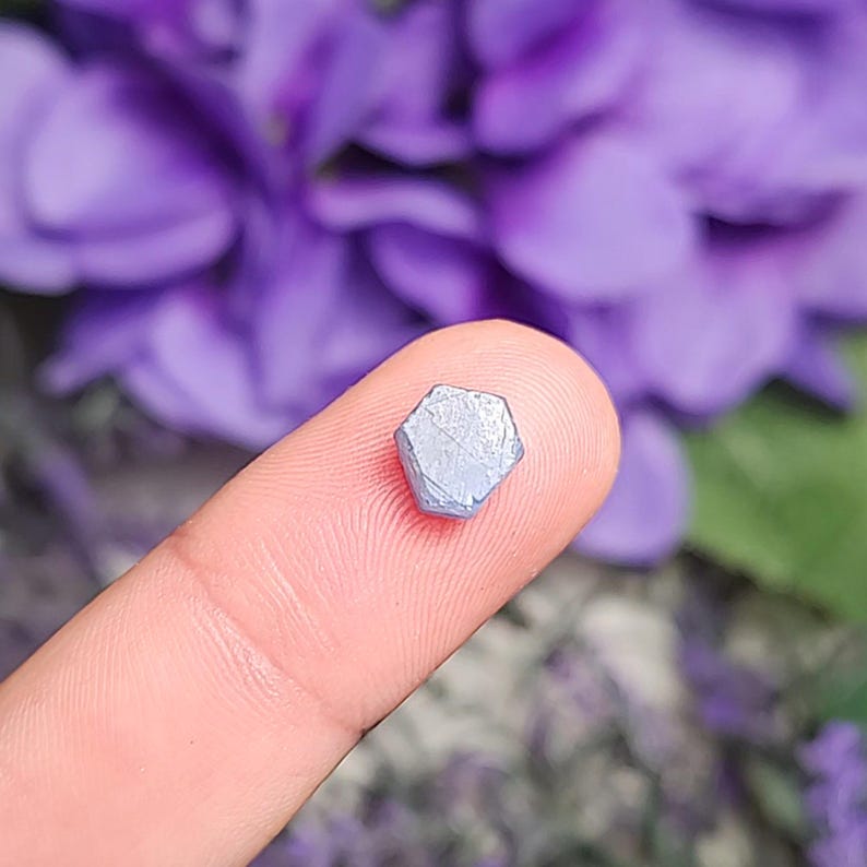 May include: A small, hexagonal, light blue sapphire crystal with a slightly iridescent sheen.