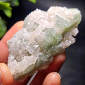 May include: A raw mineral specimen featuring a cluster of translucent, pale pinkish-white crystalline structures integrated with opaque, light sage green stone formations, showcasing a jagged, natural texture with varied geometric facets.