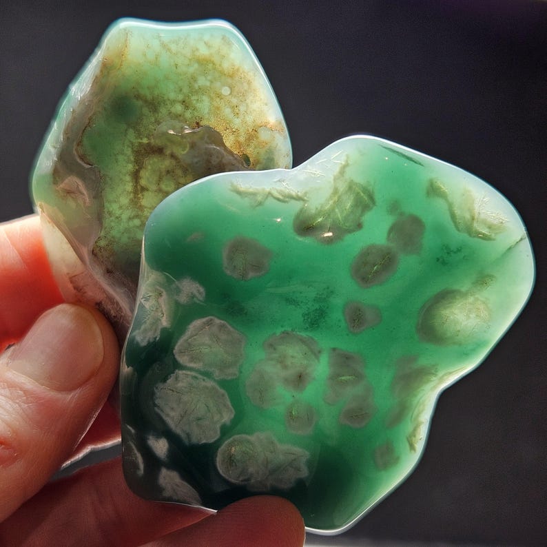 May include: Two green agate stones with white and brown inclusions. The stones are irregularly shaped and have a smooth, polished surface.