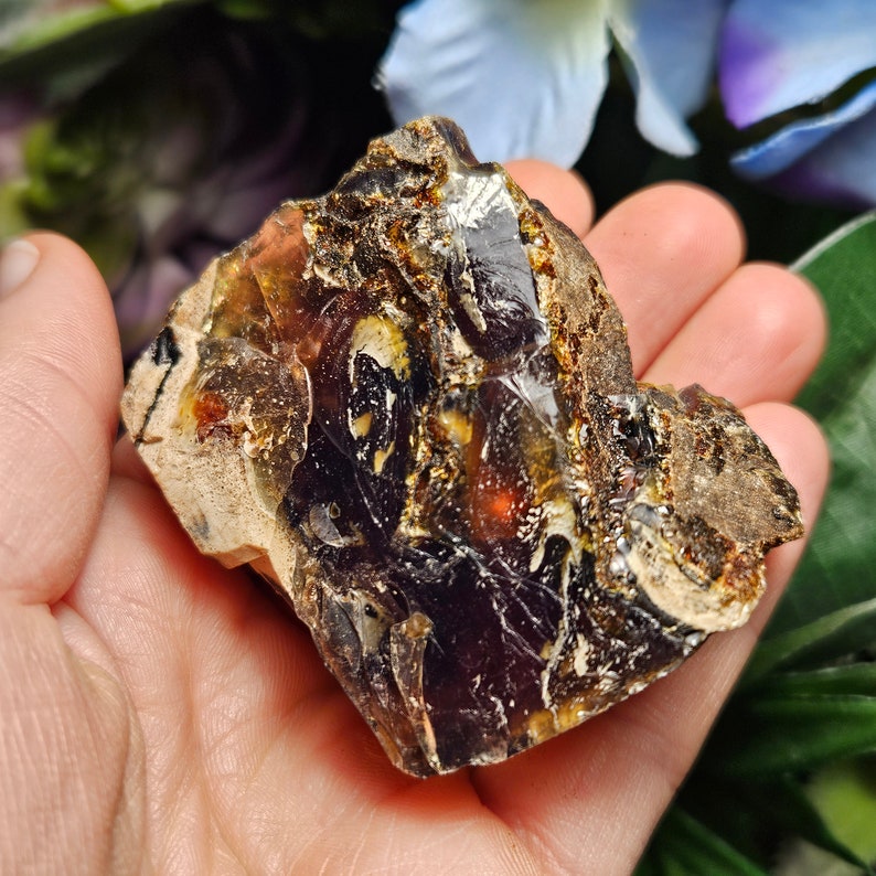 May include: A large piece of amber with a dark purple hue and inclusions of brown, yellow, and white. The amber is translucent and has a rough, natural surface.
