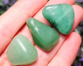 May include: Three smooth, polished green aventurine stones with a rounded, triangular shape. Each stone features a translucent, light to medium green color with subtle internal variations and a glossy, reflective surface texture.