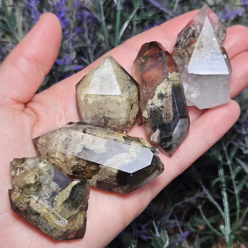 May include: A collection of raw, natural quartz crystals in various shapes and sizes. The crystals display a range of colors, including clear, brown, and smoky hues. Some crystals have visible inclusions and unique patterns, showcasing their natural beauty.