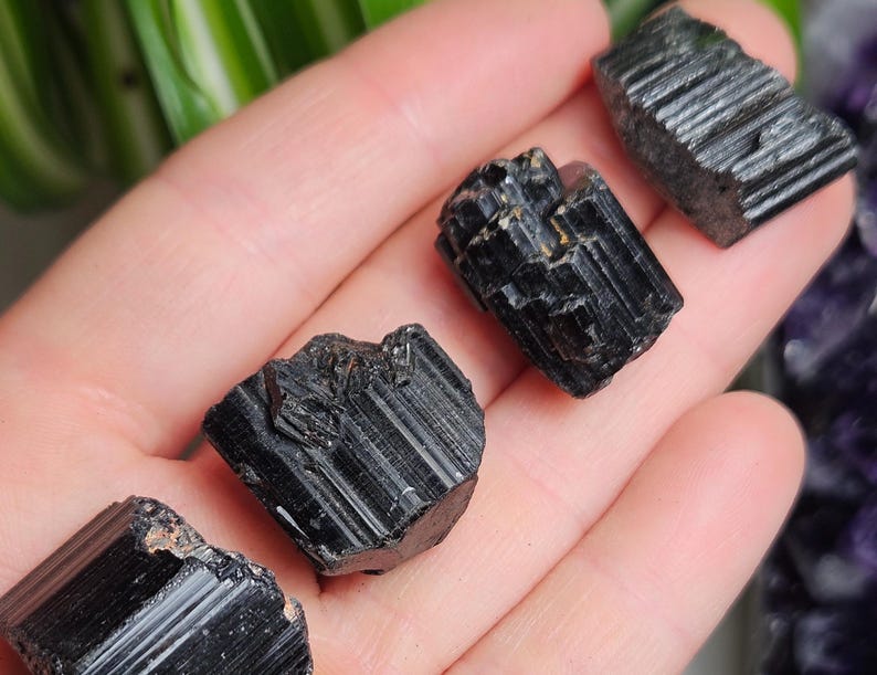 Peut inclure: Quatre cristaux de tourmaline noire brute avec des stries verticales distinctes et une finition opaque et brillante. Ces sp&eacute;cimens min&eacute;raux sombres et dentel&eacute;s pr&eacute;sentent des formes g&eacute;om&eacute;triques naturelles et des bords tranchants.