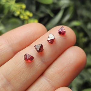 May include: Four red, faceted, natural, spinel crystals of varying sizes. The crystals are displayed on a hand.