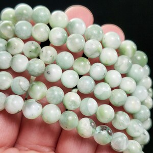 Peut inclure: Gros plan sur un chapelet de perles de pierres pr&eacute;cieuses vert clair. Les perles rondes ont un aspect translucide, avec des variations de couleur et de texture. Les perles sont tenues dans une main.
