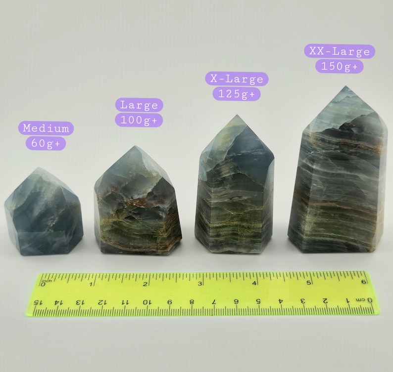 May include: Four fluorite crystal towers of varying sizes, labelled Medium (60g+), Large (100g+), X-Large (125g+), and XX-Large (150g+). The crystals are shades of green, blue, and brown. A yellow ruler is at the bottom.