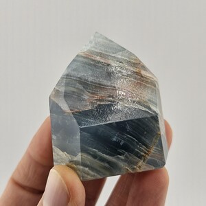 May include: A blue and brown crystal tower with a faceted design. The crystal has a layered appearance with streaks of brown and white throughout. The top of the crystal is angled, and the overall shape is geometric.