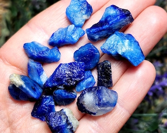 Puede incluir: Una colección de pequeñas piedras de lapislázuli ásperas, azules y blancas. Las piedras son de varias formas y tamaños.