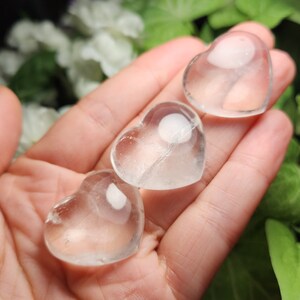 May include: Three clear quartz crystal hearts in the shape of a heart. The hearts are smooth and polished.