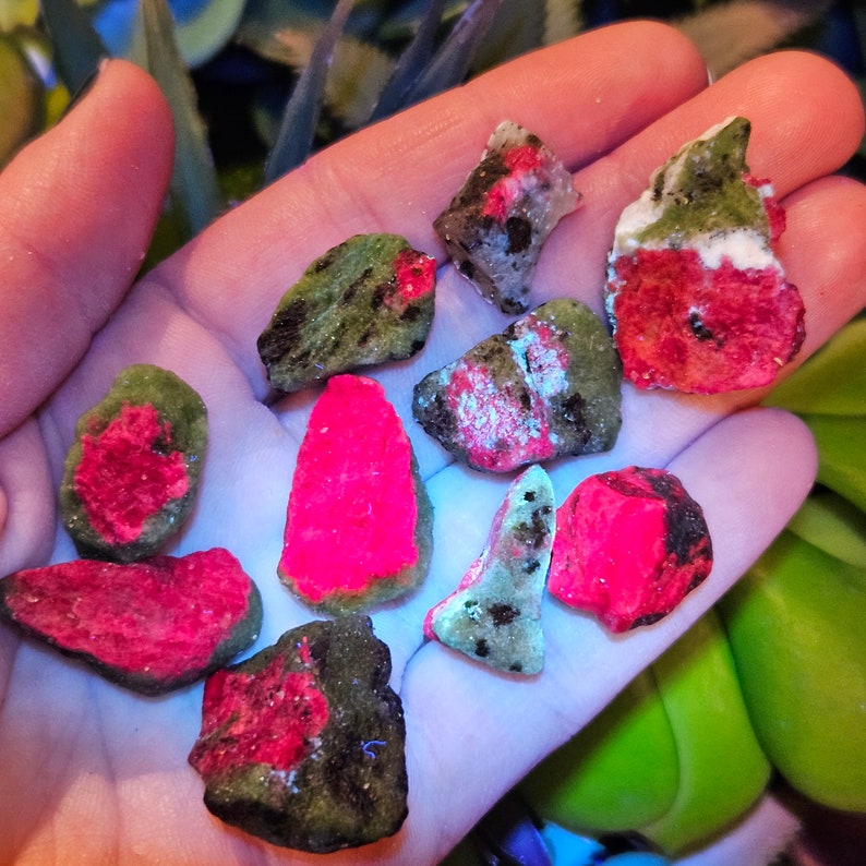 Pu&ograve; includere: Una collezione di pietre preziose grezze, non tagliate, con un contrasto cromatico sorprendente. Le pietre presentano un esterno verde scuro con interni rosa e rossi neon vibranti. Alcune pietre hanno un aspetto maculato bianco e nero.